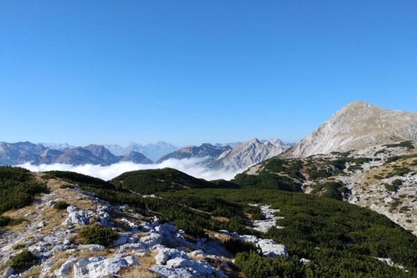 Skalnat gorski svet z ruševjem in pasom oblakov v dolini